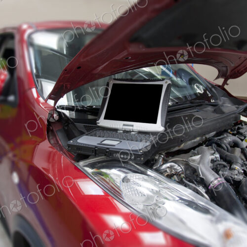 Car in a workshop and a computer running diagnostics on the engine.