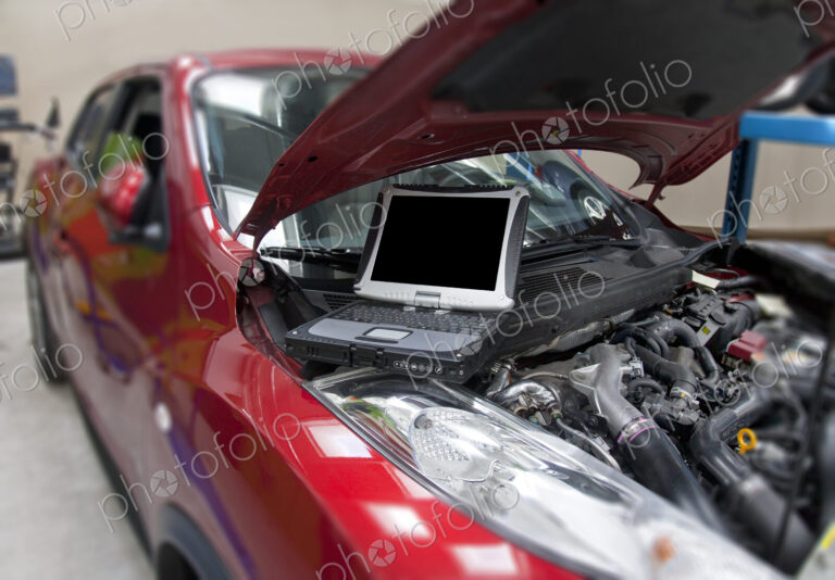 Car in a workshop and a computer running diagnostics on the engine.