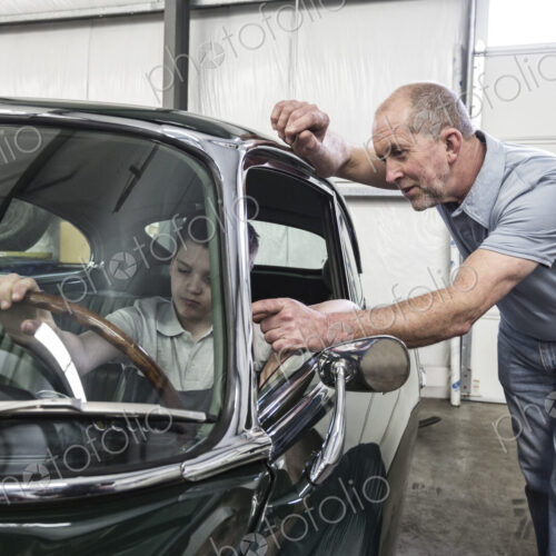 Car mechanic and a small boy sitting in the driving seat of an old classic car.