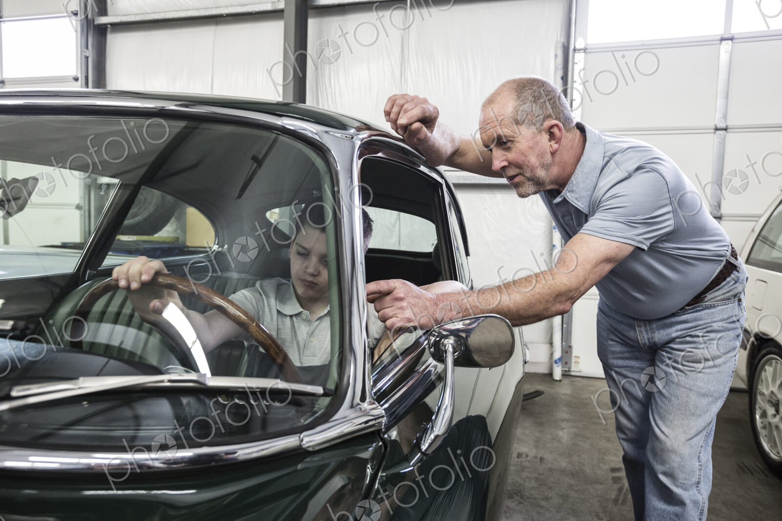 Car mechanic and a small boy sitting in the driving seat of an old classic car.