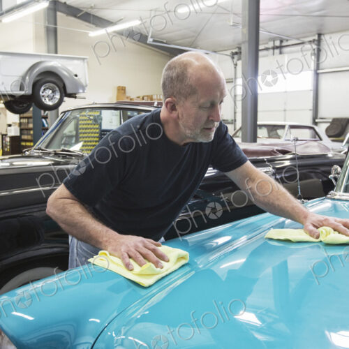 Car mechanic applying wax to the hood of an old sedan in classic car repair shop. Car mechanic applying wax to the hood of an old sedan in classic car repair shop.