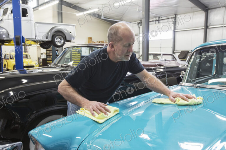 Car mechanic applying wax to the hood of an old sedan in classic car repair shop.