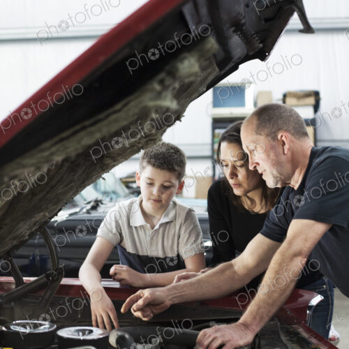 Car mechanic talks to a mother and her son about a engine repair issue in classic car…