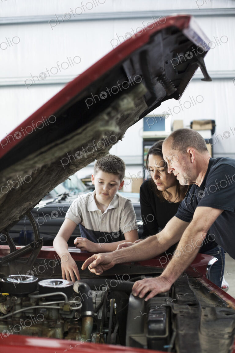 Car mechanic talks to a mother and her son about a engine repair issue in classic car…