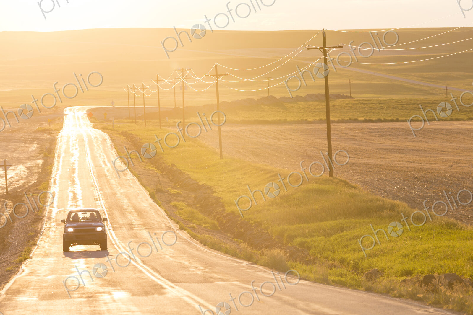Car traveling on long straight open highway at sunset.