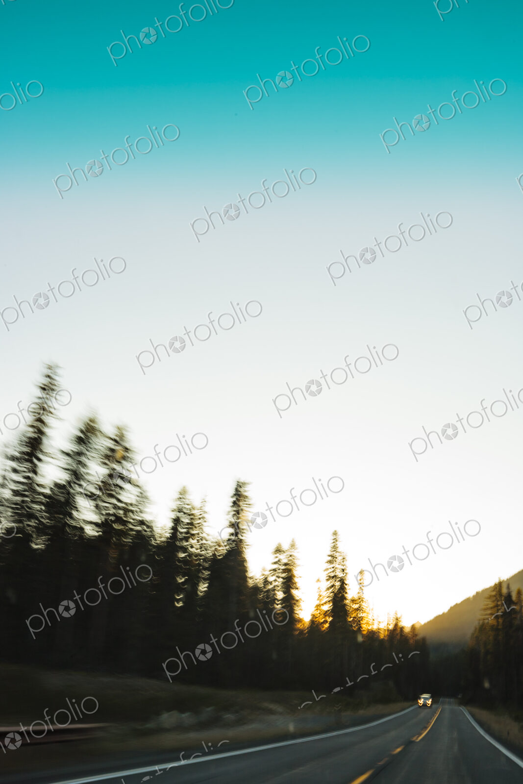 Car with headlights driving on a rural mountain highway at dusk.