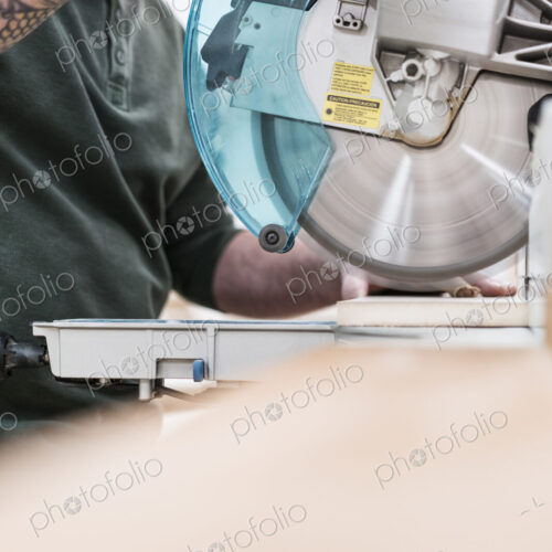 Carpenter using a radial saw to cut a wooden board in a woodworking factory.