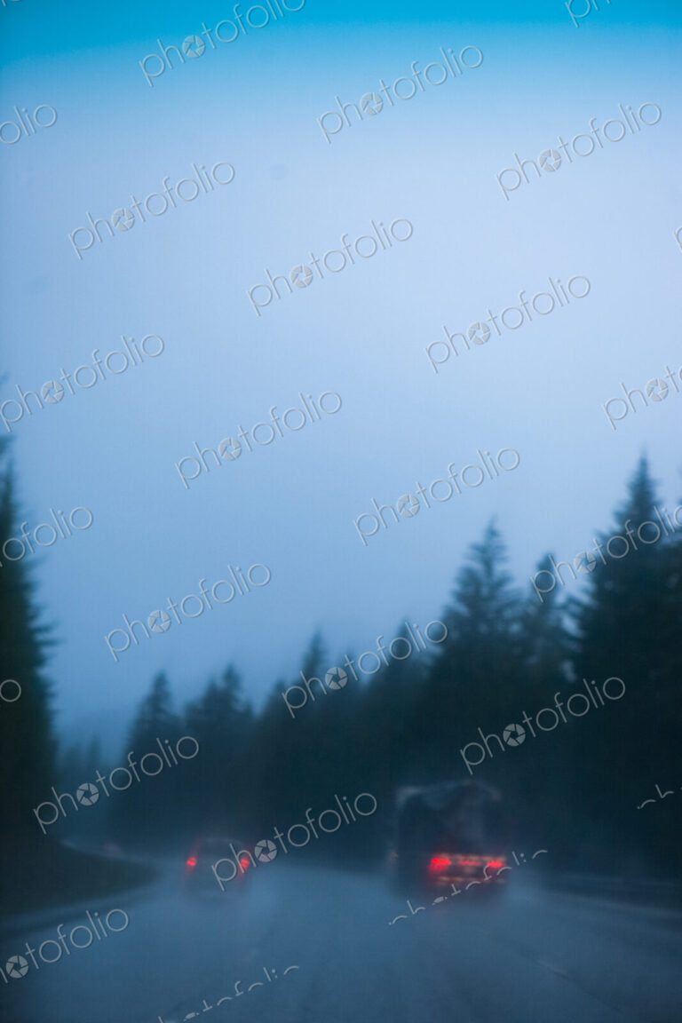 Cars and truck driving in heavy rain on a road through a forest, Snoqualmie Pass, WA, USA