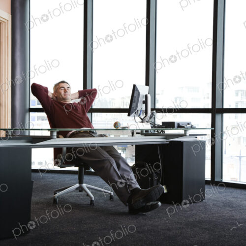 Casually dressed caucasian businessman relaxed at his desk in front of a large bank of… Casually dressed caucasian businessman relaxed at his desk in front of a large bank of…