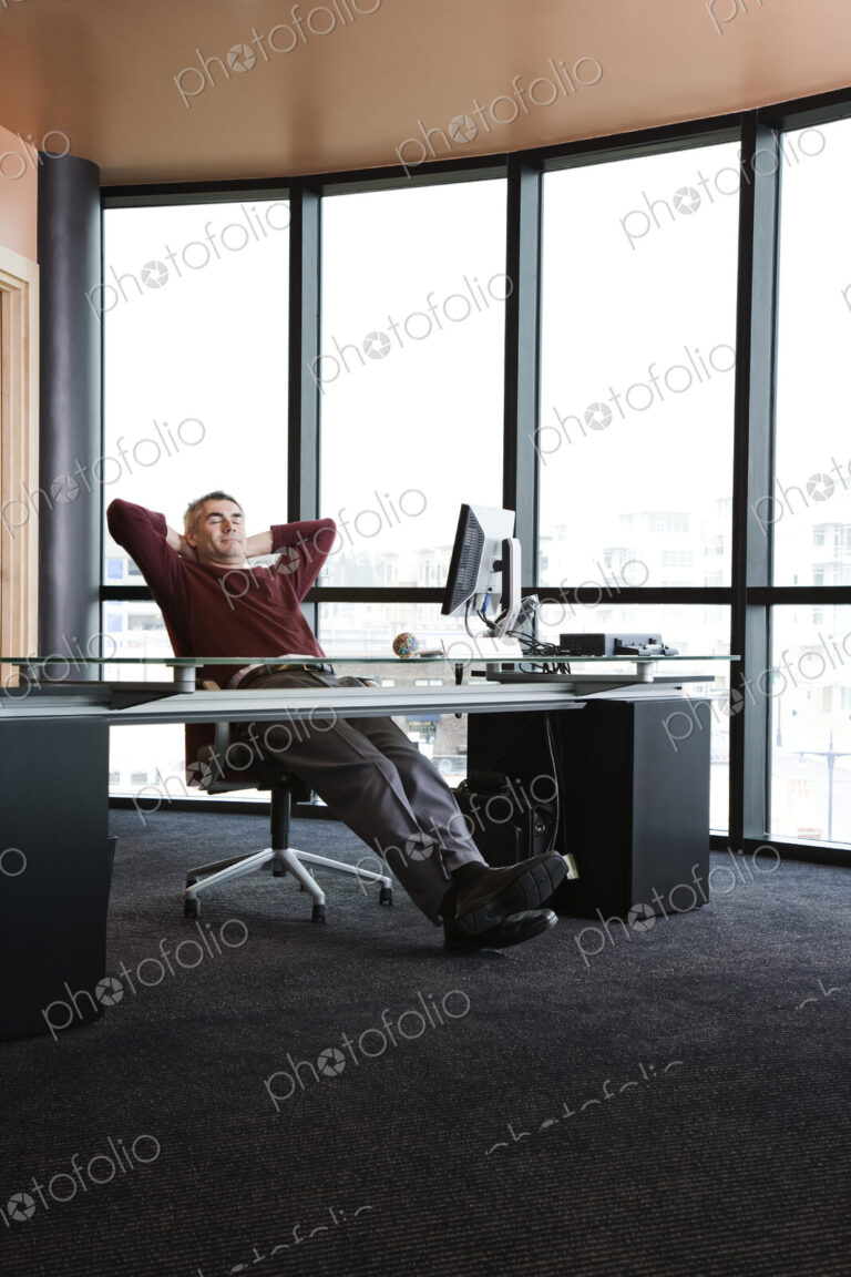 Casually dressed caucasian businessman relaxed at his desk in front of a large bank of…