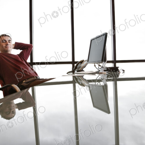 Casually dressed caucasian businessman relaxed at his reflective desk in front of a… Casually dressed caucasian businessman relaxed at his reflective desk in front of a…
