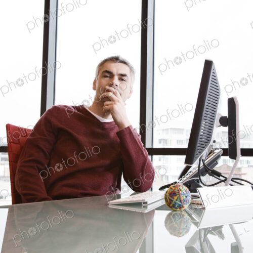 Casually dressed caucasian businessman relaxed at his reflective desk in front of a… Casually dressed caucasian businessman relaxed at his reflective desk in front of a…