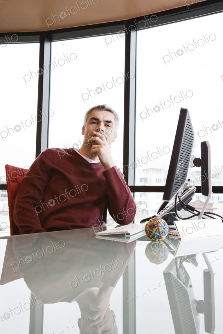 Casually dressed caucasian businessman relaxed at his reflective desk in front of a…