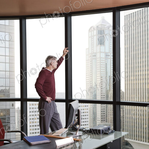 Casually dressed caucasian businessman standing and looking at a skyline out an office…