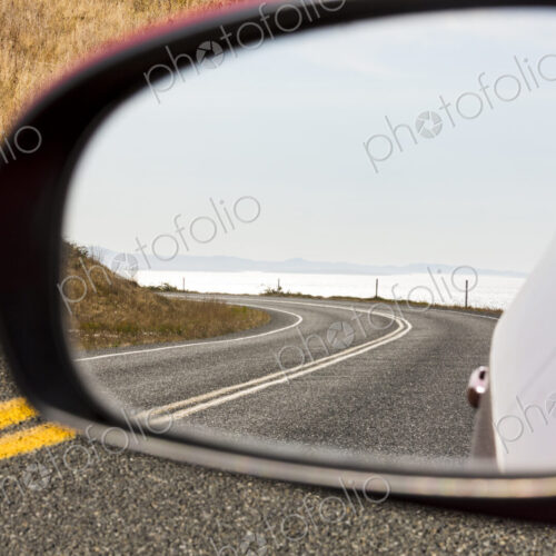Cattle Pass Road, a curving road along the coast, view in the rear view mirror. Cattle Pass Road, a curving road along the coast, view in the rear view mirror.