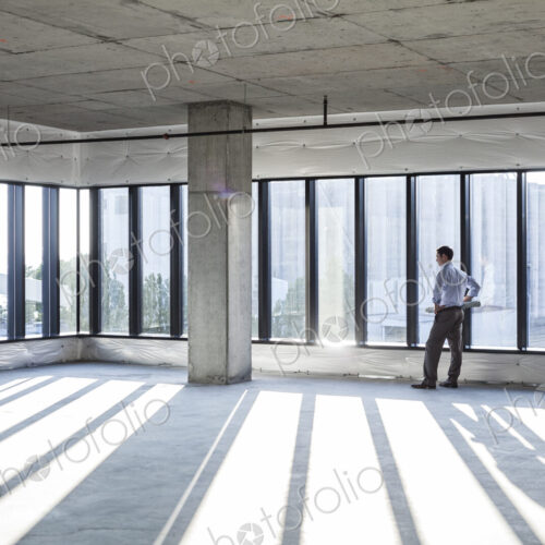 Caucaisan businessman carrying plans and looking at a new empty raw office space.