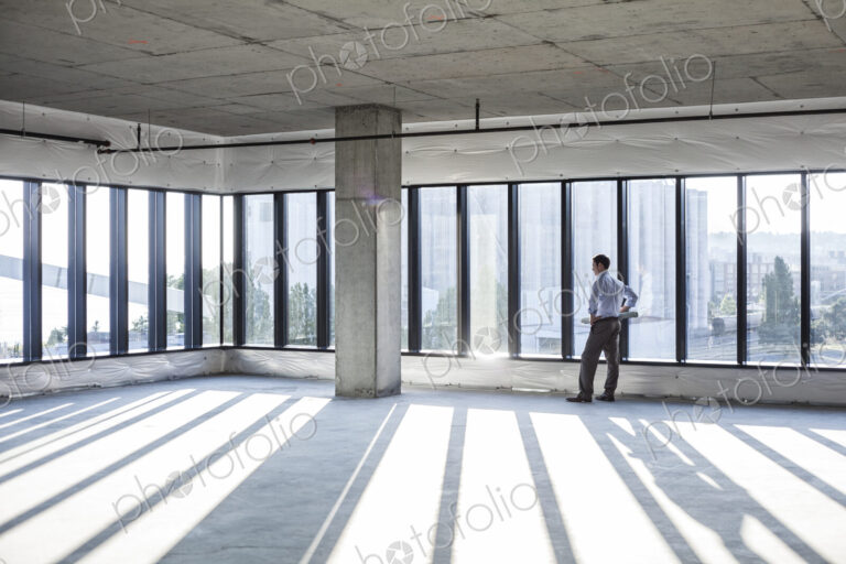 Caucaisan businessman carrying plans and looking at a new empty raw office space.