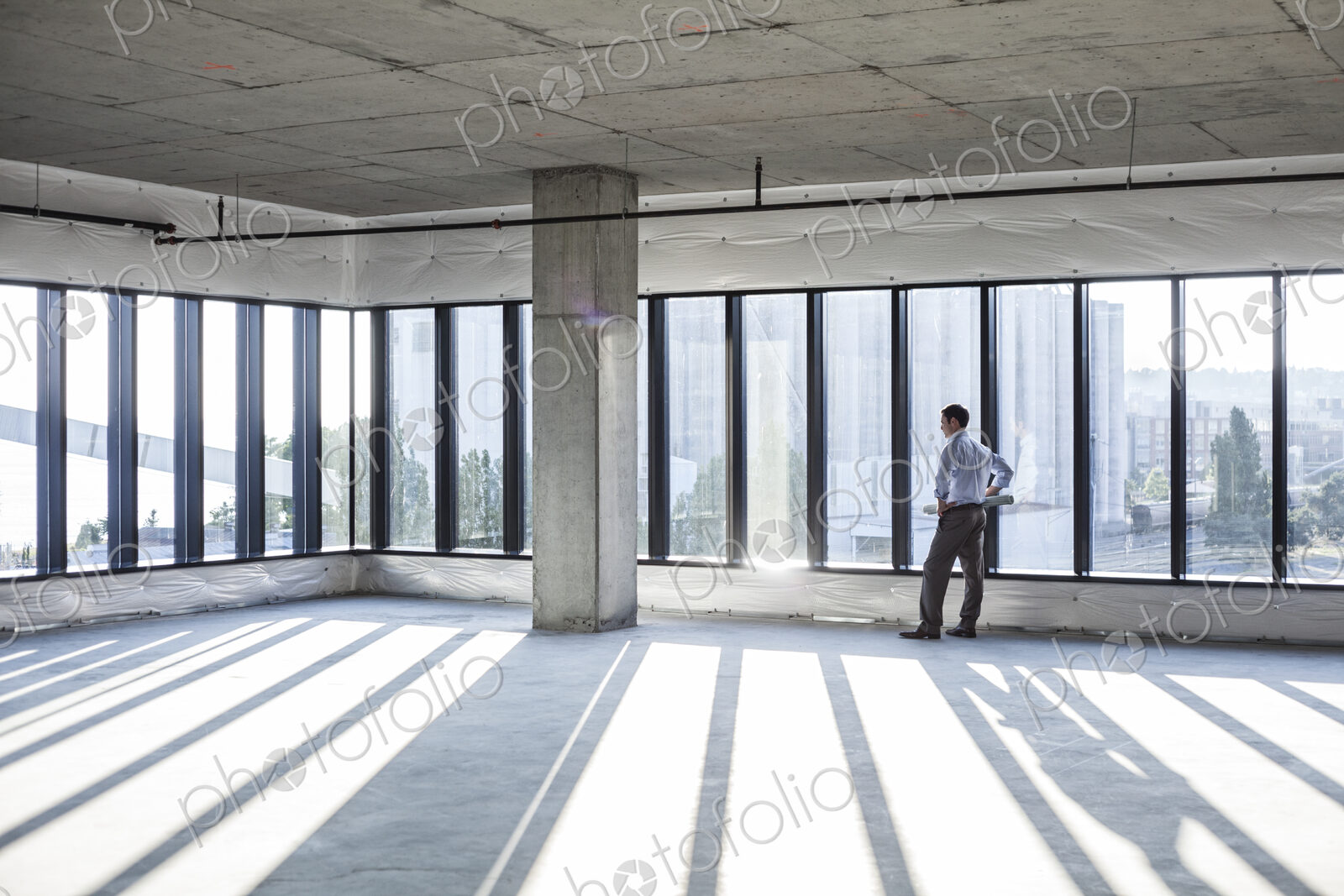 Caucaisan businessman carrying plans and looking at a new empty raw office space.