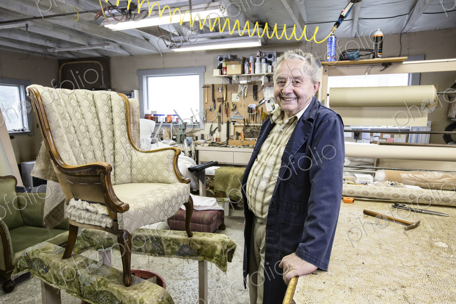 Caucaisan senior male upholsterer working on a chair in his garage shop.