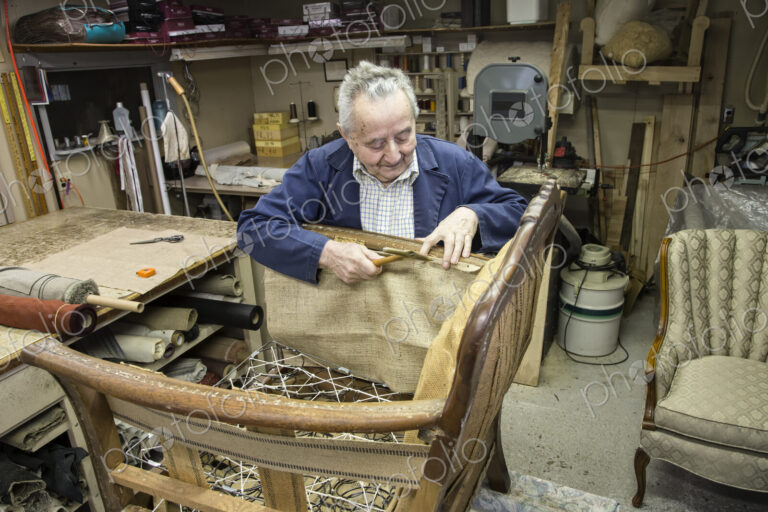 Caucaisan senior male upholsterer working on a chair in his garage shop.