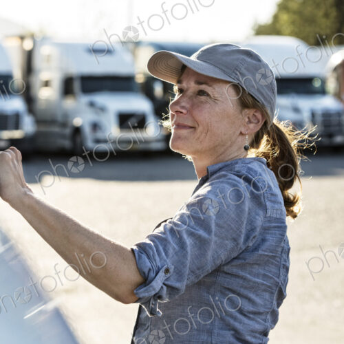Caucasan female truck driver getting into her truck parked in a lot at a truck stop. Caucasan female truck driver getting into her truck parked in a lot at a truck stop.