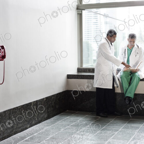 Caucasian and black men doctors conferring over a medical record in a hospital hallway.