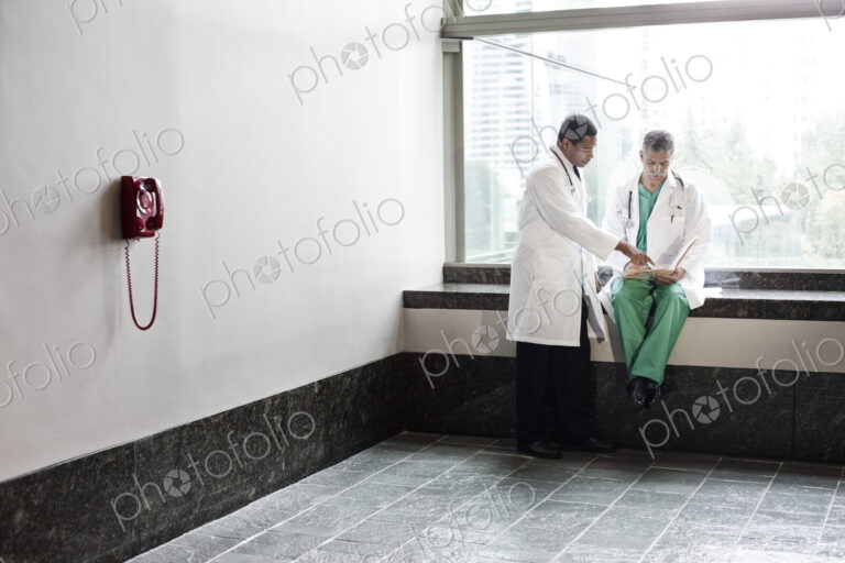 Caucasian and black men doctors conferring over a medical record in a hospital hallway.