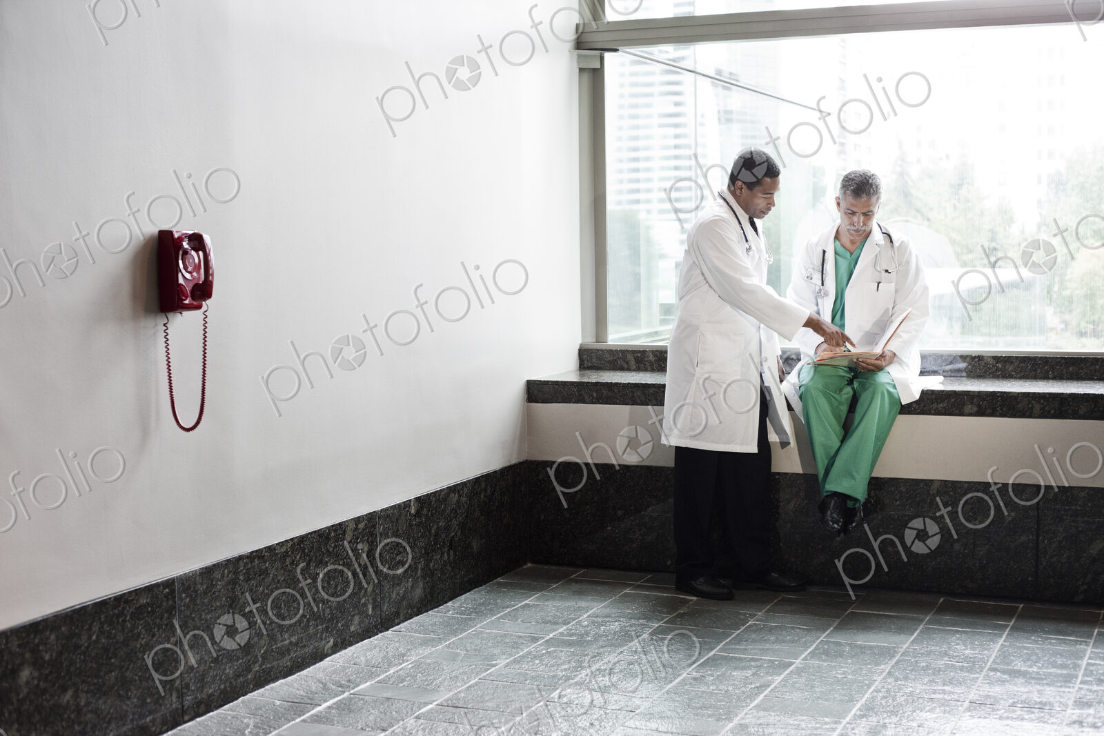 Caucasian and black men doctors conferring over a medical record in a hospital hallway.