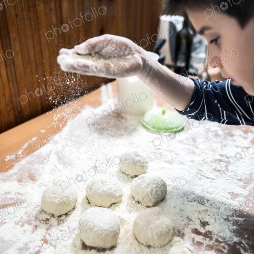 Caucasian boy sprinkling flour over dough balls