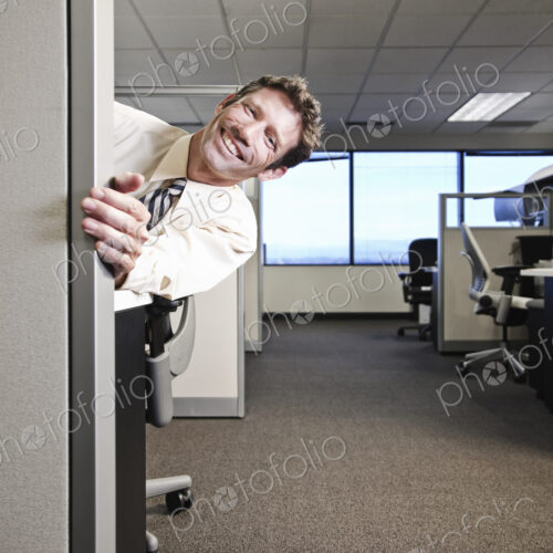 Caucasian businesman smiling and looking around the corner of his office cubicle. Caucasian businesman smiling and looking around the corner of his office cubicle.