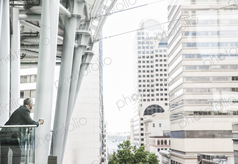 Caucasian business man standing on a balcony overlooking a cityscape.