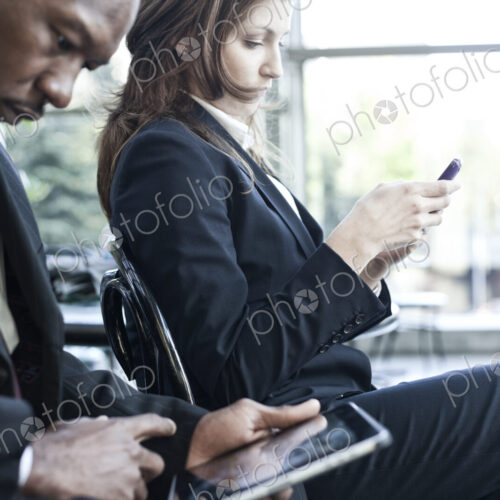 Caucasian business woman texting mear a black businessman who is on a notebook computer. Caucasian business woman texting mear a black businessman who is on a notebook computer.