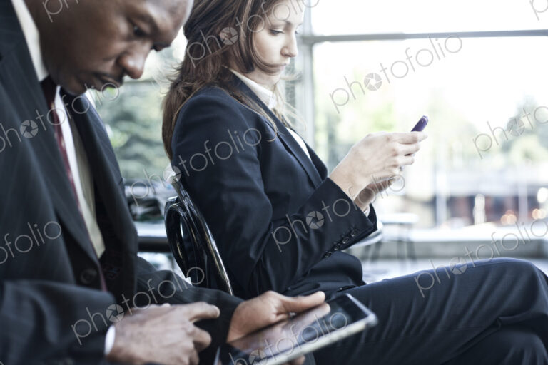 Caucasian business woman texting mear a black businessman who is on a notebook computer.