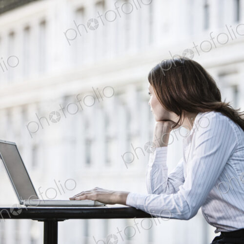 Caucasian business woman working on a laptop computer at a table in a lobby waiting area.