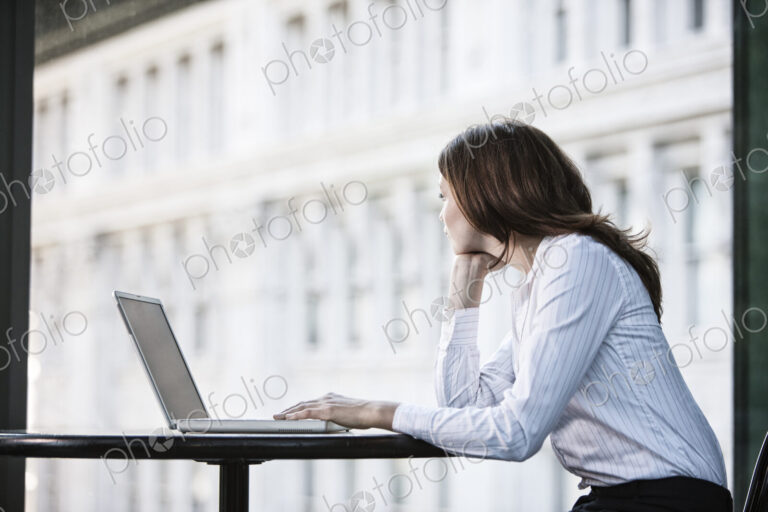 Caucasian business woman working on a laptop computer at a table in a lobby waiting area.