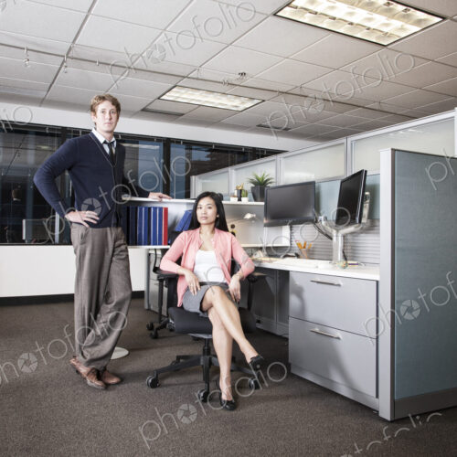 Caucasian businessman and Asian businesswoman team of people in a cubicle office space. Caucasian businessman and Asian businesswoman team of people in a cubicle office space.