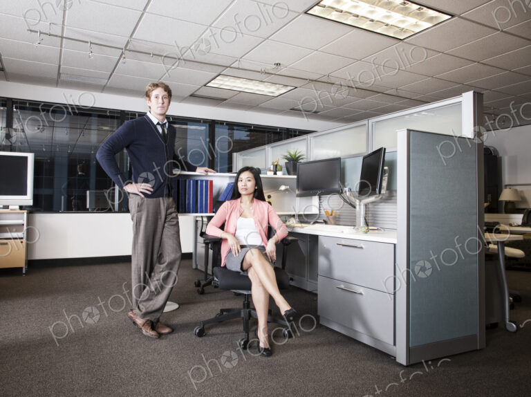 Caucasian businessman and Asian businesswoman team of people in a cubicle office space.