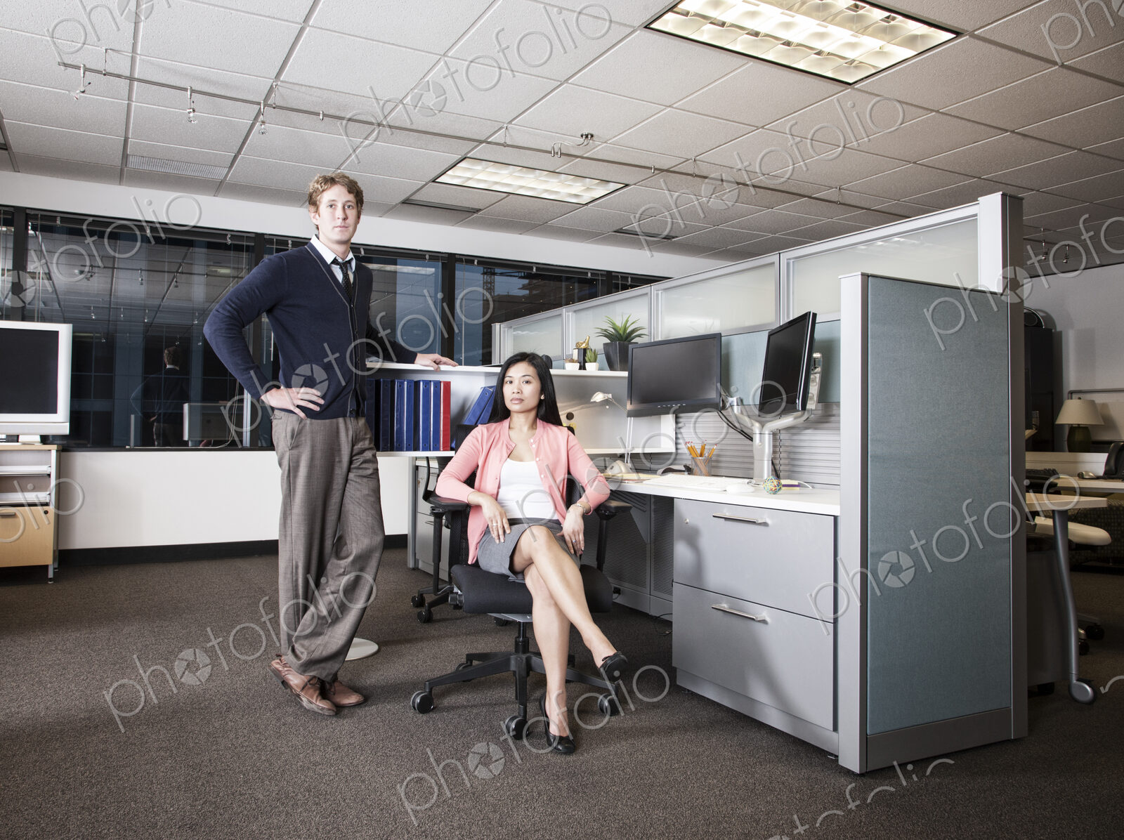 Caucasian businessman and Asian businesswoman team of people in a cubicle office space.