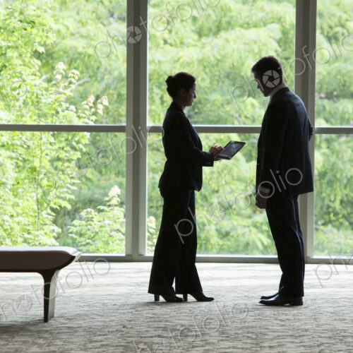 Caucasian businessman and woman looking at a computer notebook in front of a large… Caucasian businessman and woman looking at a computer notebook in front of a large…