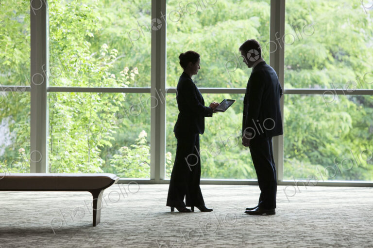Caucasian businessman and woman looking at a computer notebook in front of a large…