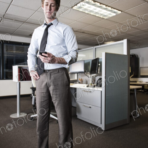 Caucasian businessman checking a text on his cell phone standing in his cubicle office. Caucasian businessman checking a text on his cell phone standing in his cubicle office.