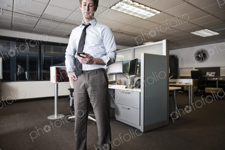 Caucasian businessman checking a text on his cell phone standing in his cubicle office.