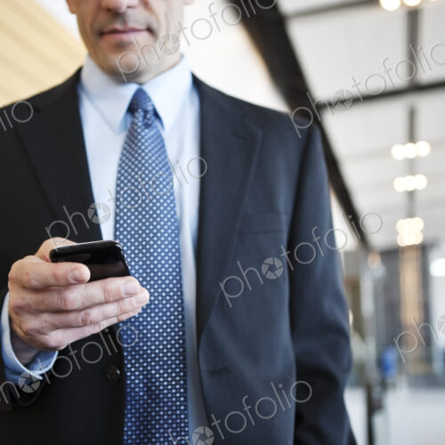 Caucasian businessman checking his cell phone in a conference centre lobby.