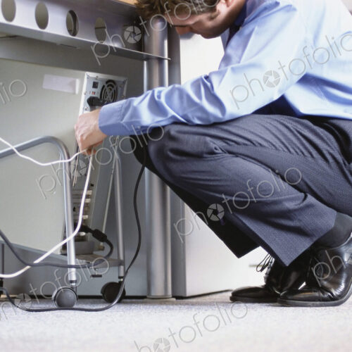 Caucasian businessman connecting cables to computer in office Caucasian businessman connecting cables to computer in office
