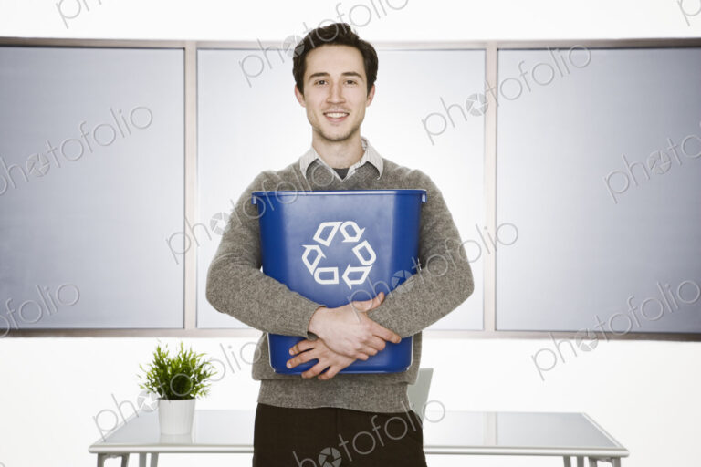Caucasian businessman holding a recyle wast basket in his office.