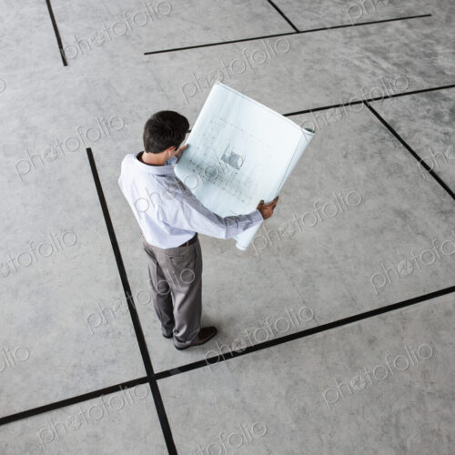 Caucasian businessman holding plans for a new office in a large empty raw office space.