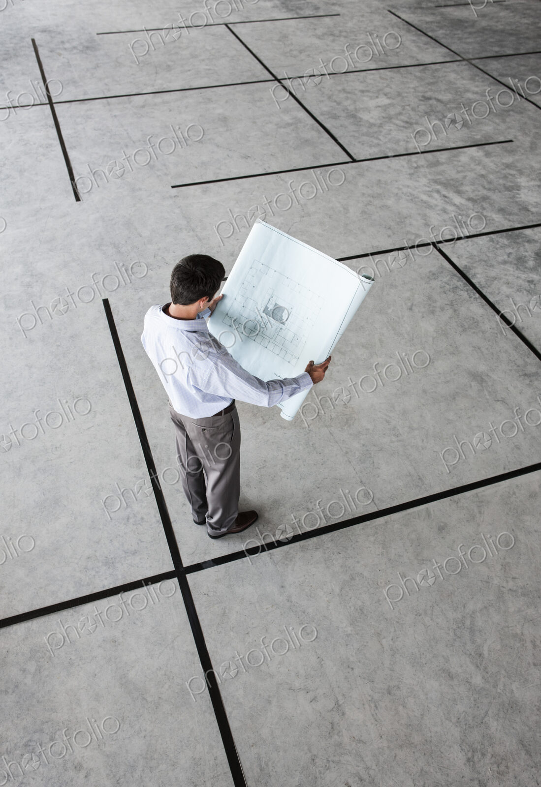 Caucasian businessman holding plans for a new office in a large empty raw office space.
