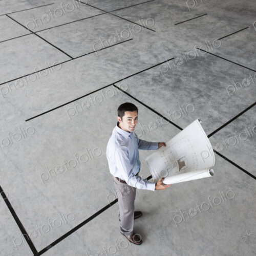Caucasian businessman holding plans for a new office in a large empty raw office space.