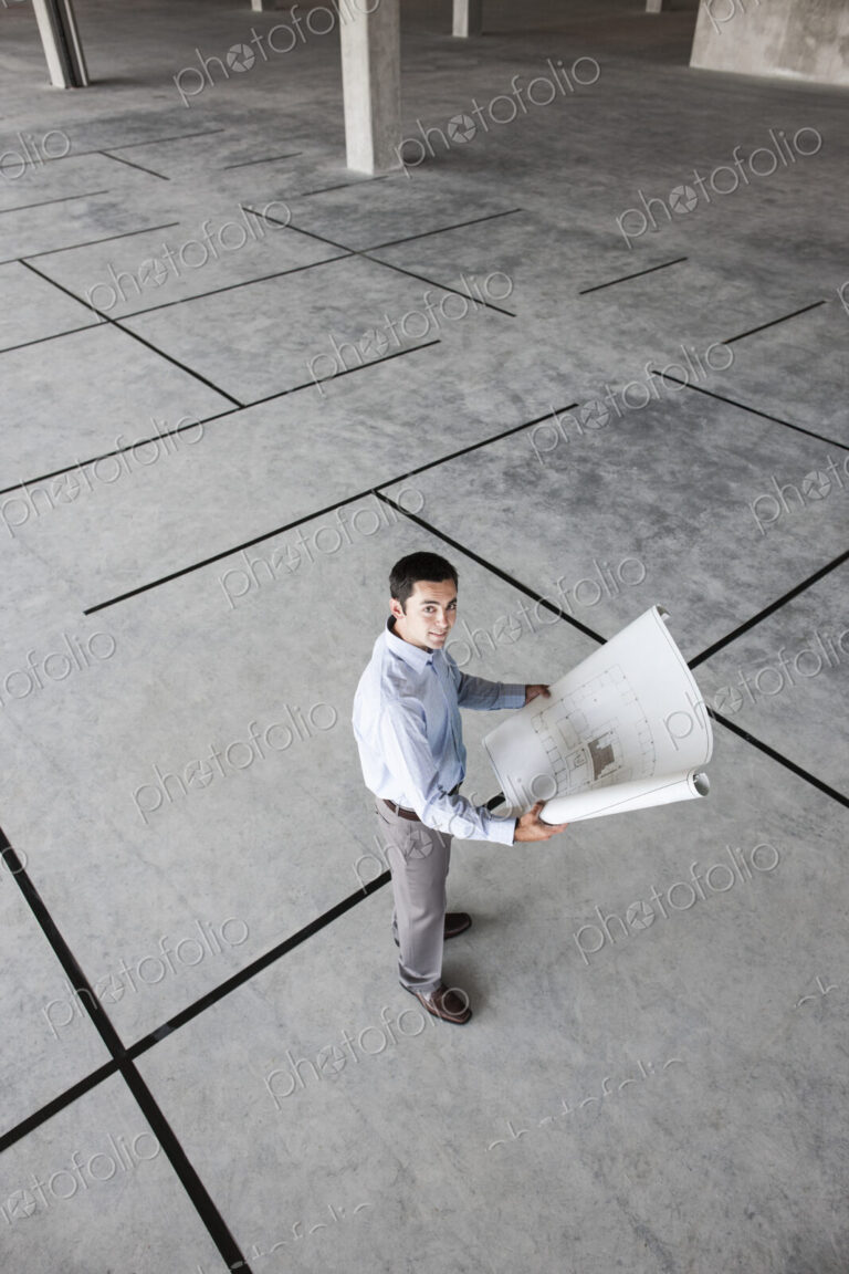Caucasian businessman holding plans for a new office in a large empty raw office space.