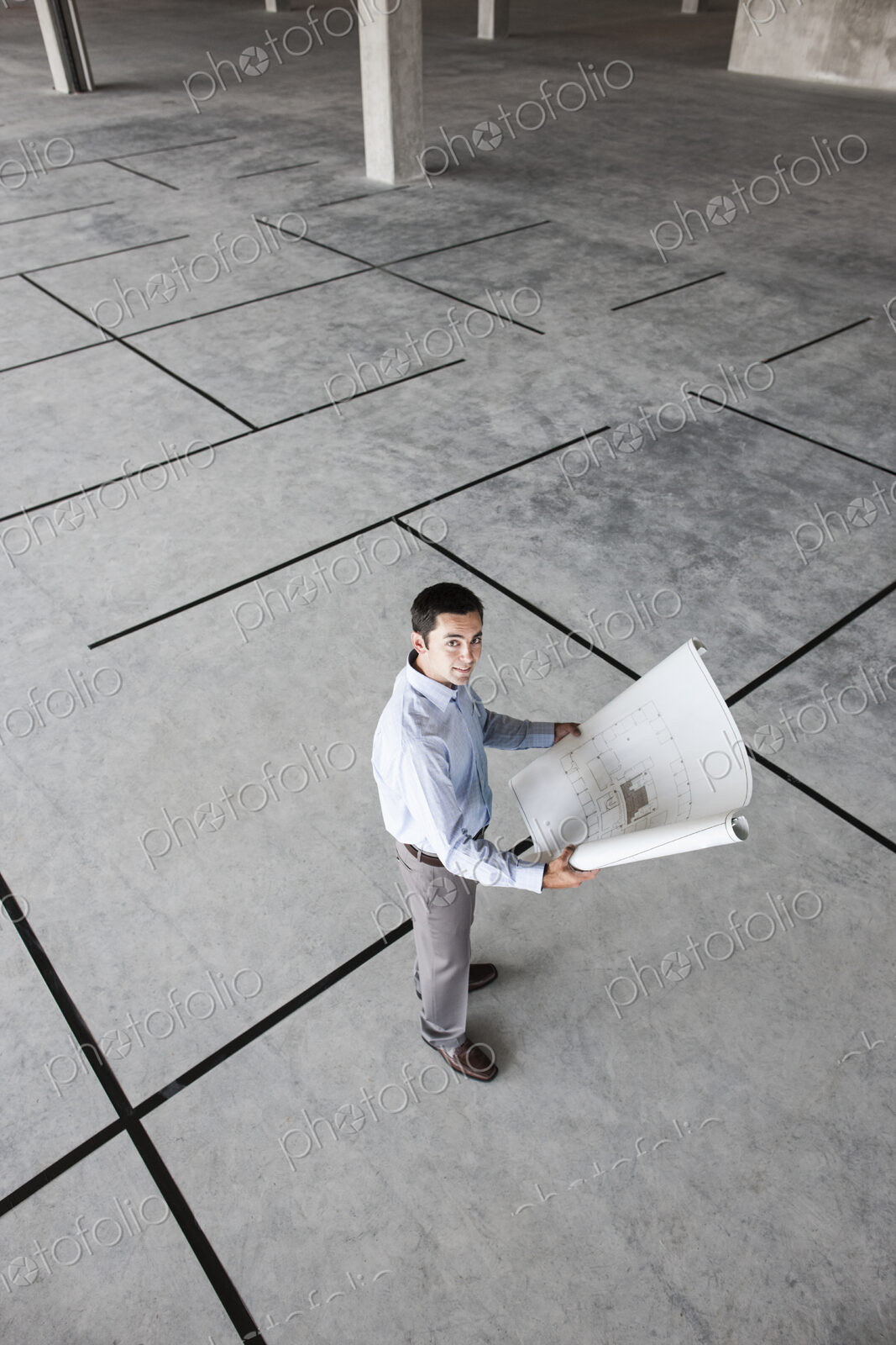 Caucasian businessman holding plans for a new office in a large empty raw office space.